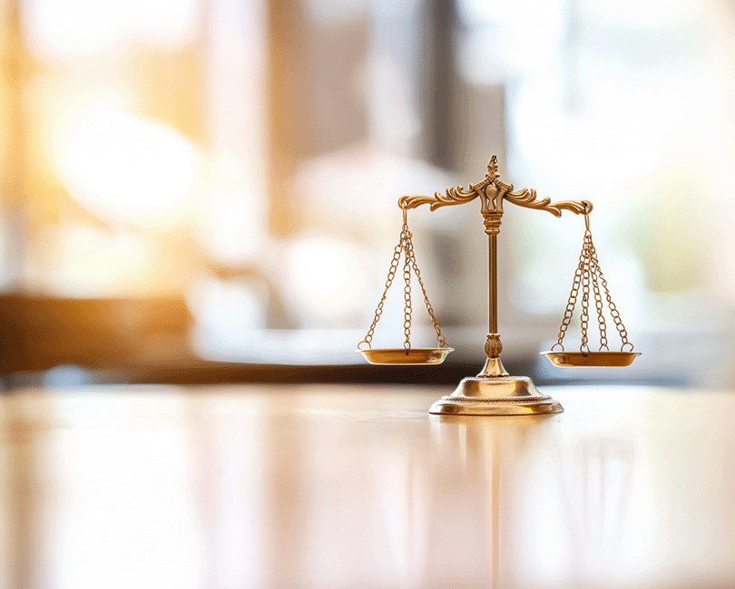 A golden balance scale on a smooth surface, set against a blurred background with warm, bright tones. The ornate and symmetrical scale symbolizes justice, much like the equitable distribution found in well-structured pay bands.